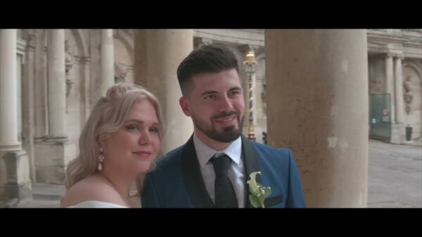 Couple en tenue de mariage souriant, architecture classique.