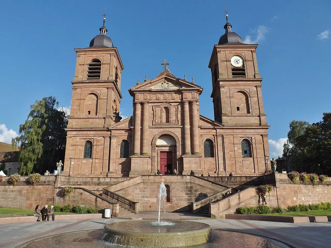 Église avec fontaine devant, ciel bleu.