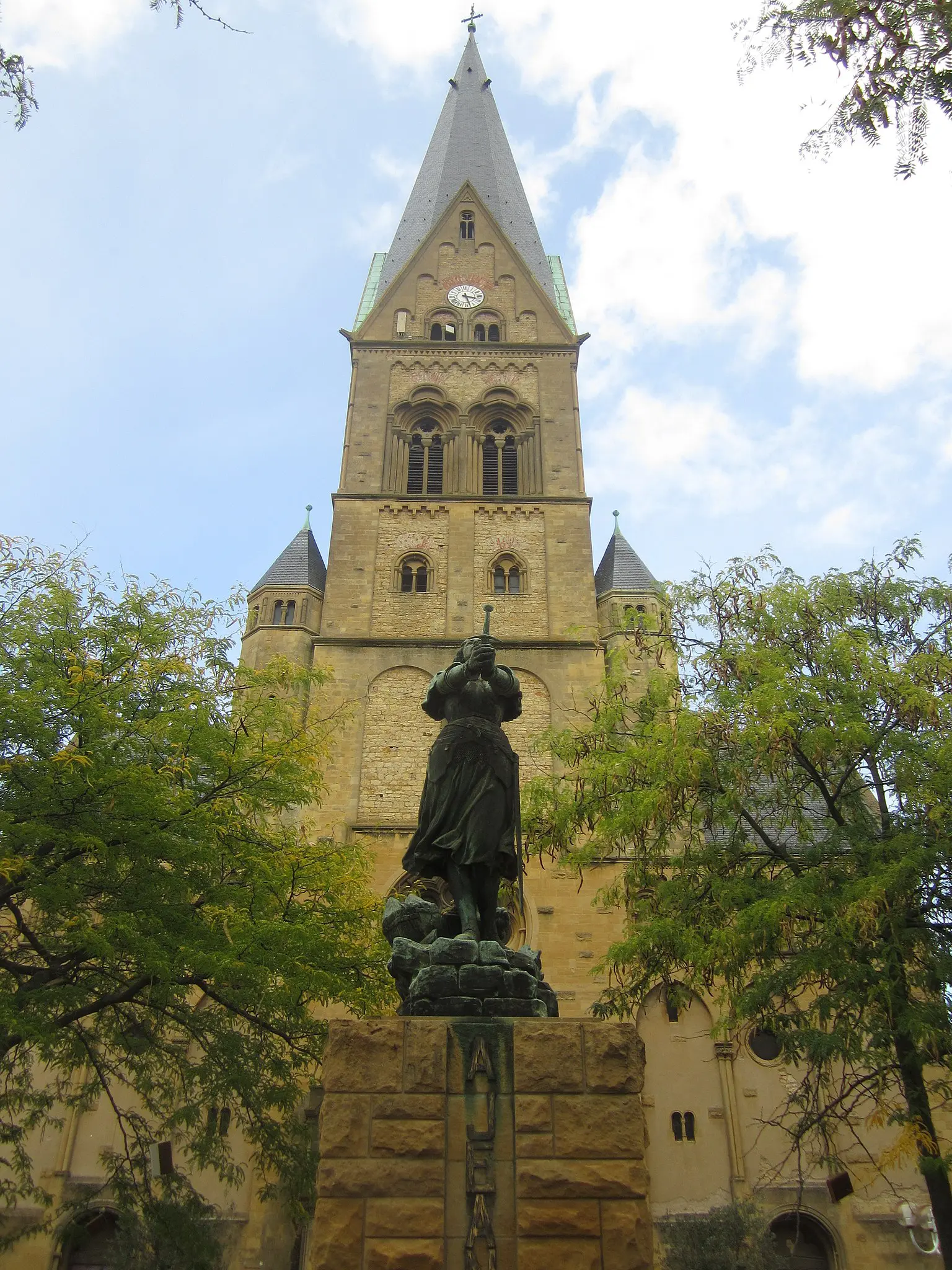 Statue devant église gothique, ciel nuageux.